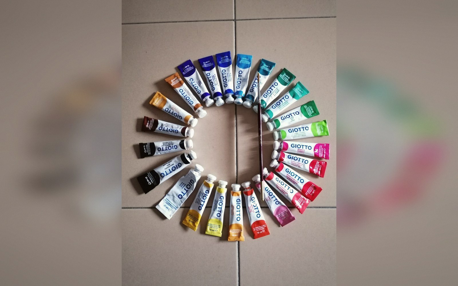 Giotto paint tubes arranged in a color wheel with a paintbrush across the center