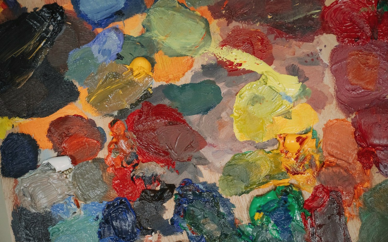Thick daubs of mixed oil paint colors clustered together on an artist's palette